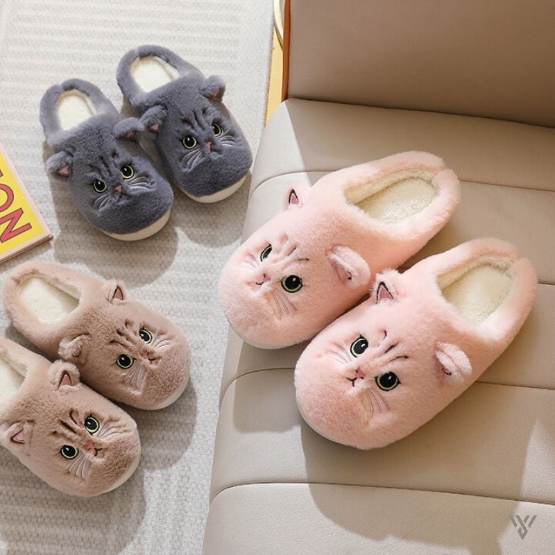 Pair of pink cat-shaped slippers on a beige couch with another pair of gray cat-shaped slippers on a textured surface.
