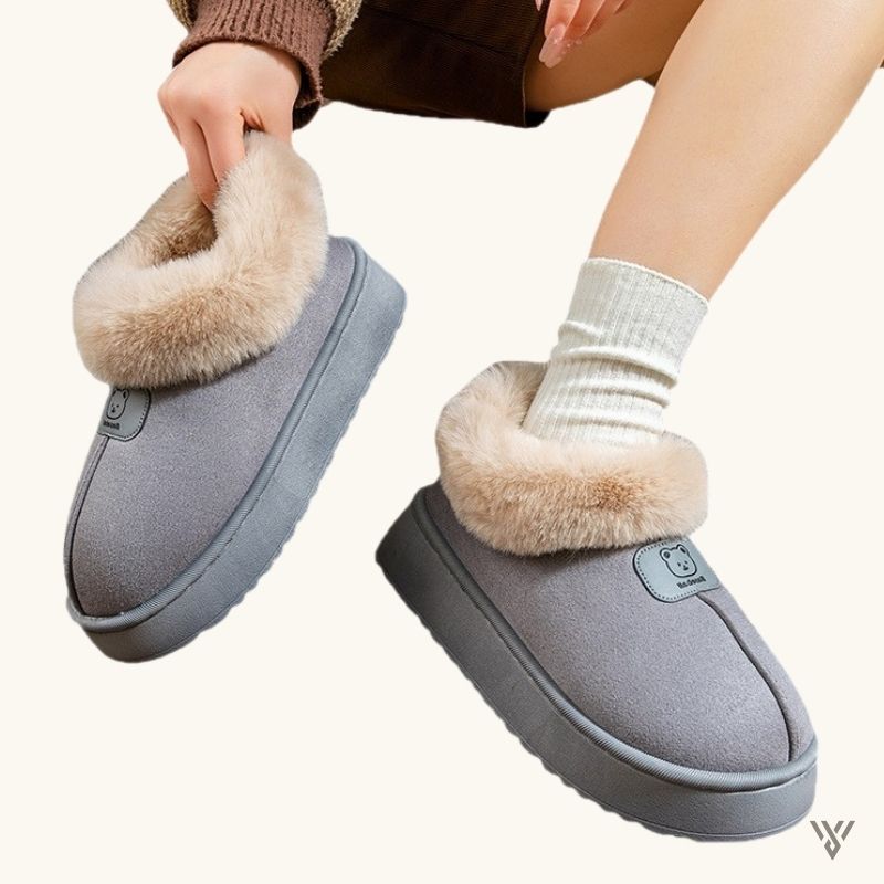 Gray slippers with fur trim worn by a person on a white background